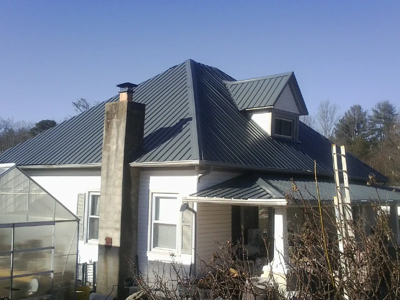 Dark blue standing seam metal roof on a white farmhouse with dormer — Slate & Tile Roof Repair by Roofing Brothers in Lenoir