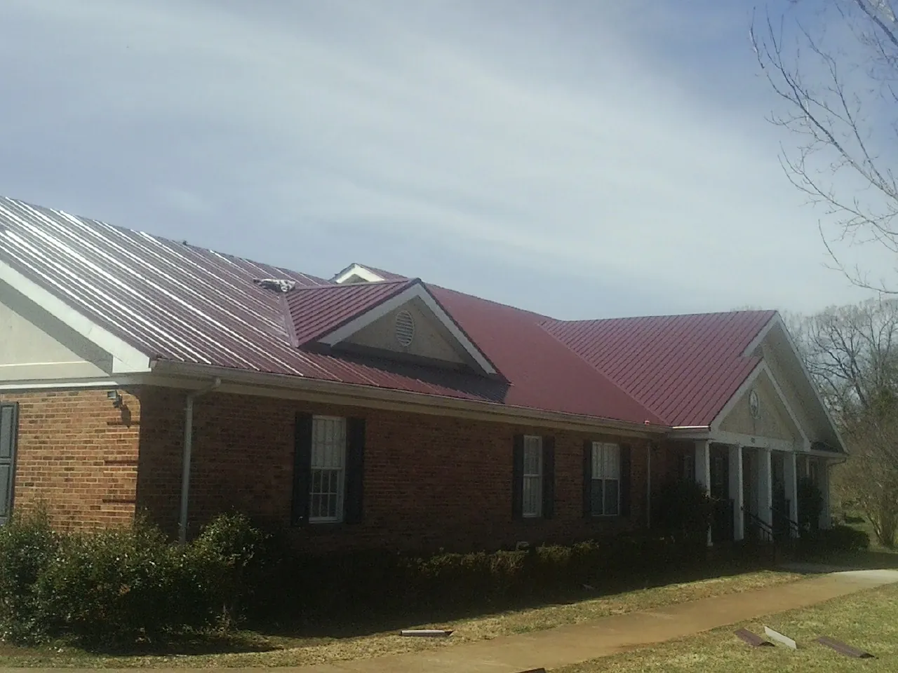 Red metal roof with gabled entries on a long brick building, from a Hail Damage Roof Repair job in Lenoir