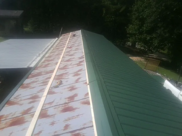 Old rusted panels beside newly installed green metal roofing — Wind Damage Roof Repair by Roofing Brothers in Lenoir