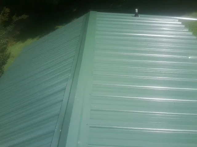 New green metal panels meeting at the ridge of a roof — Flat Roof Repair work by our crew in Lenoir