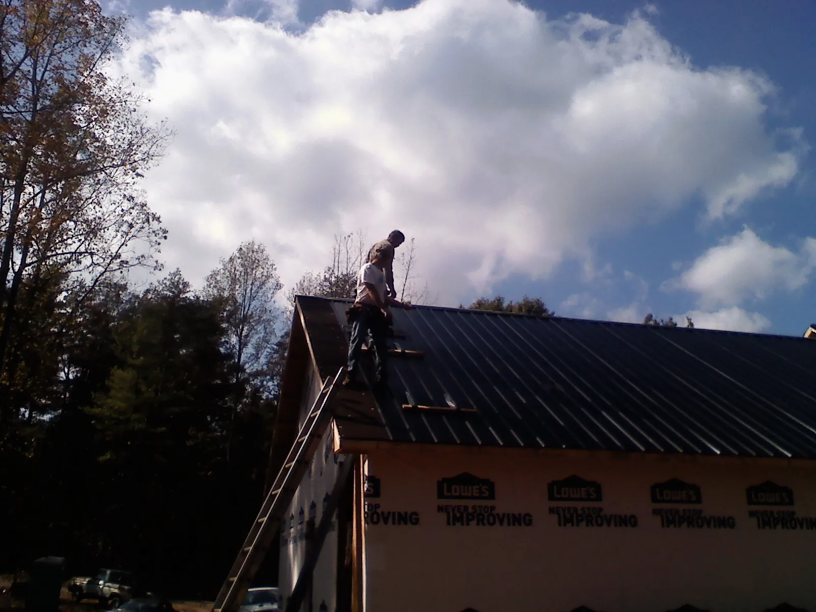 Roofer fastening dark metal panels high against a cloudy sky, from a Roof Inspection job in Lenoir