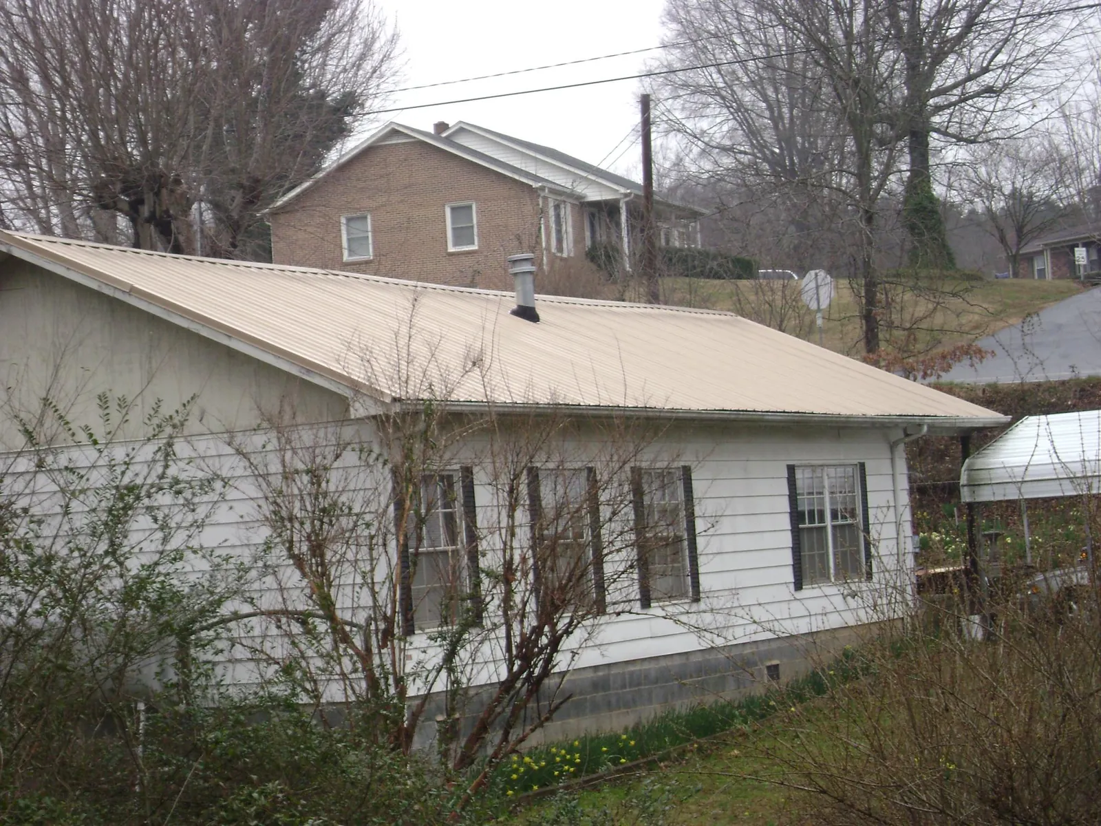 Tan metal roof on a white sided house set into a hillside — Commercial Roofing by Roofing Brothers in Lenoir