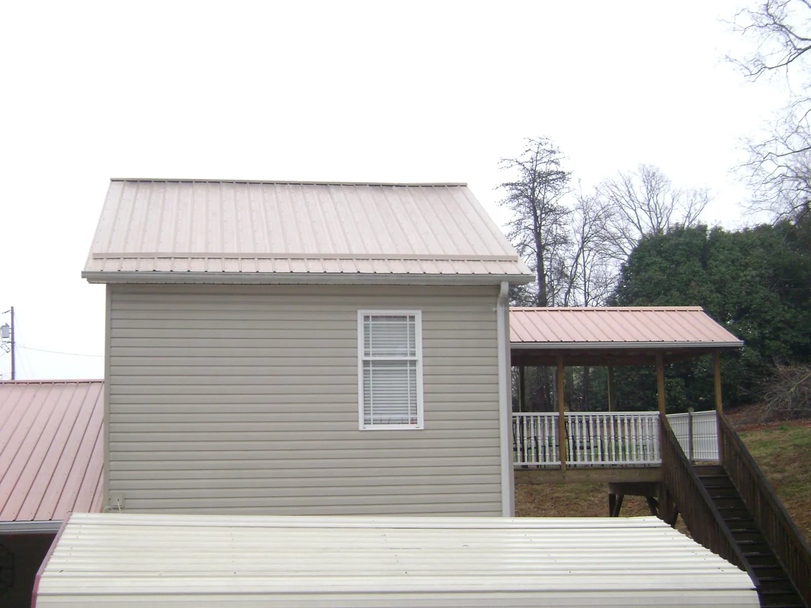 Tan metal roofs on a two story addition and attached porch, from a Roof Replacement job in Lenoir