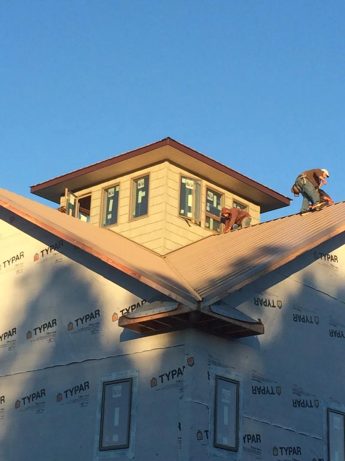 Roofers working around a rooftop cupola on a new metal roof at sunset — Roof Waterproofing in Lenoir by Roofing Brothers